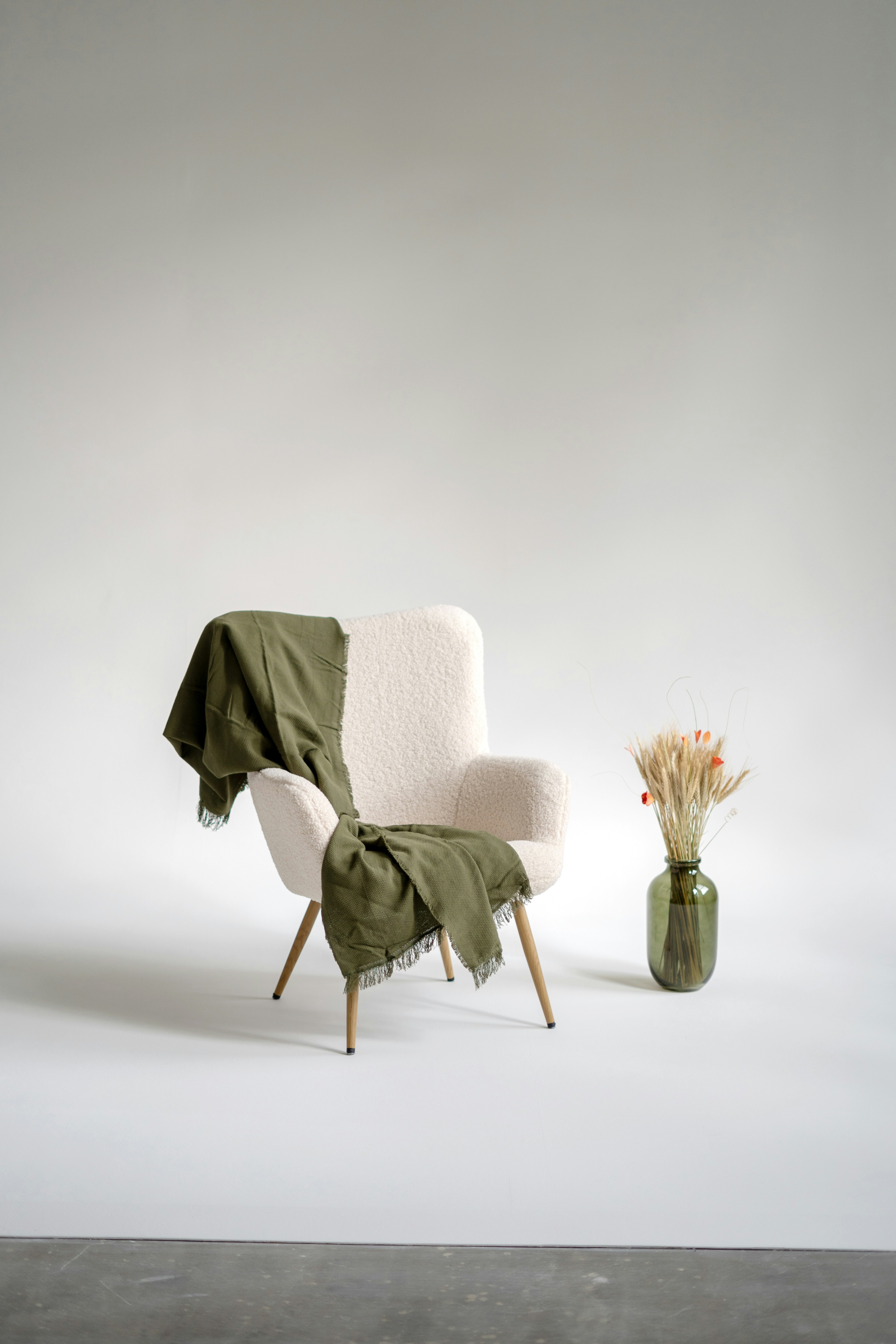 Cream armchair with an olive throw on a grey studio sweep
